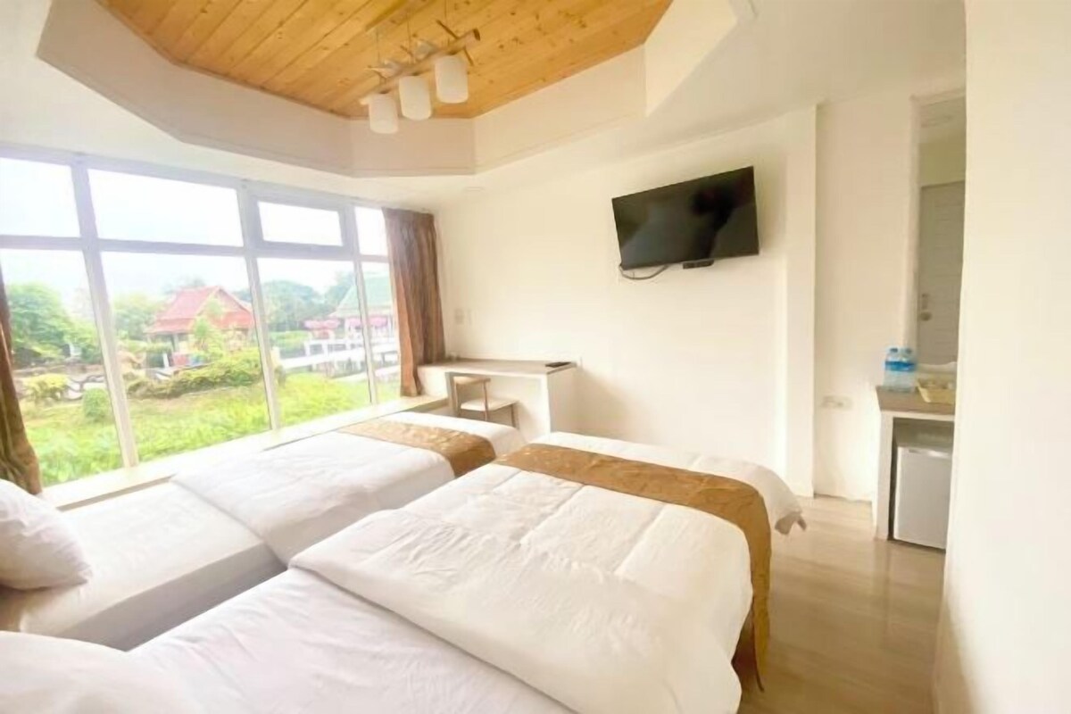 Ein Hotelzimmer mit zwei Betten, einem an der Wand befestigten Fernseher und Blick auf Grünflächen.