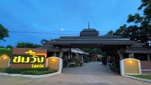 L’entrée d’un hôtel, avec une enseigne en langue étrangère, une allée couverte et, au fond, une structure traditionnelle rappelant une pagode.