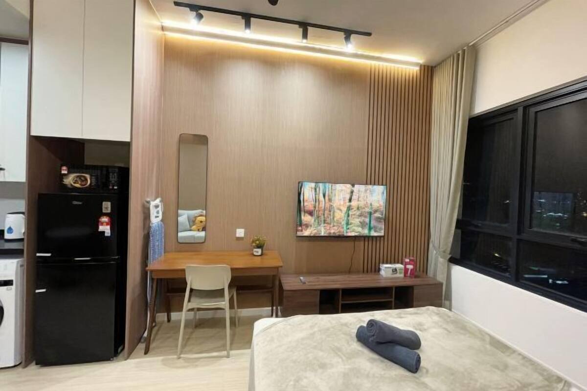 Ein kleines Hotelzimmer mit Bett, Schreibtisch, Stuhl, einer kleinen Küchenzeile und einem großen Fenster.