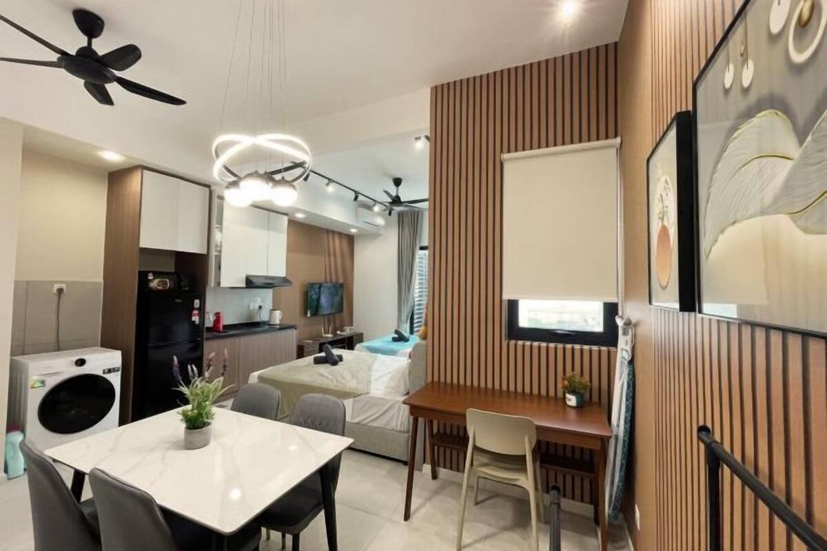 A compact living space with a dining area, kitchenette, and a bedroom with a bed and curtains.