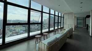 A modern interior with large windows, wicker furniture, and a city view. - The Pano at Jalan Ipoh Near KLCC By The Homez (Kuala Lumpur)