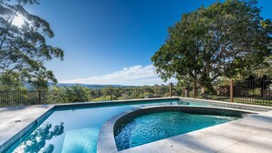 A swimming pool with a curved edge, surrounded by a tiled deck and a metal fence. - Casa Vista- House With A View. A Unique Spanish Style Home (Ilkley)