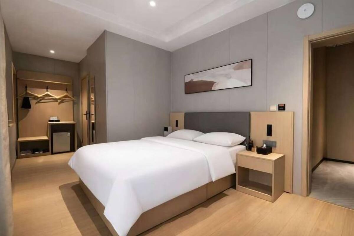 A modern hotel room with a large bed, bedside tables, a wardrobe, and a painting on the wall.