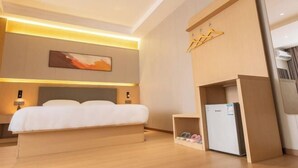 Une chambre d’hôtel moderne dotée d’un grand lit, de lampes de chevet, d’une œuvre d’art accrochée au mur, d’une armoire intégrée et d’un petit réfrigérateur.