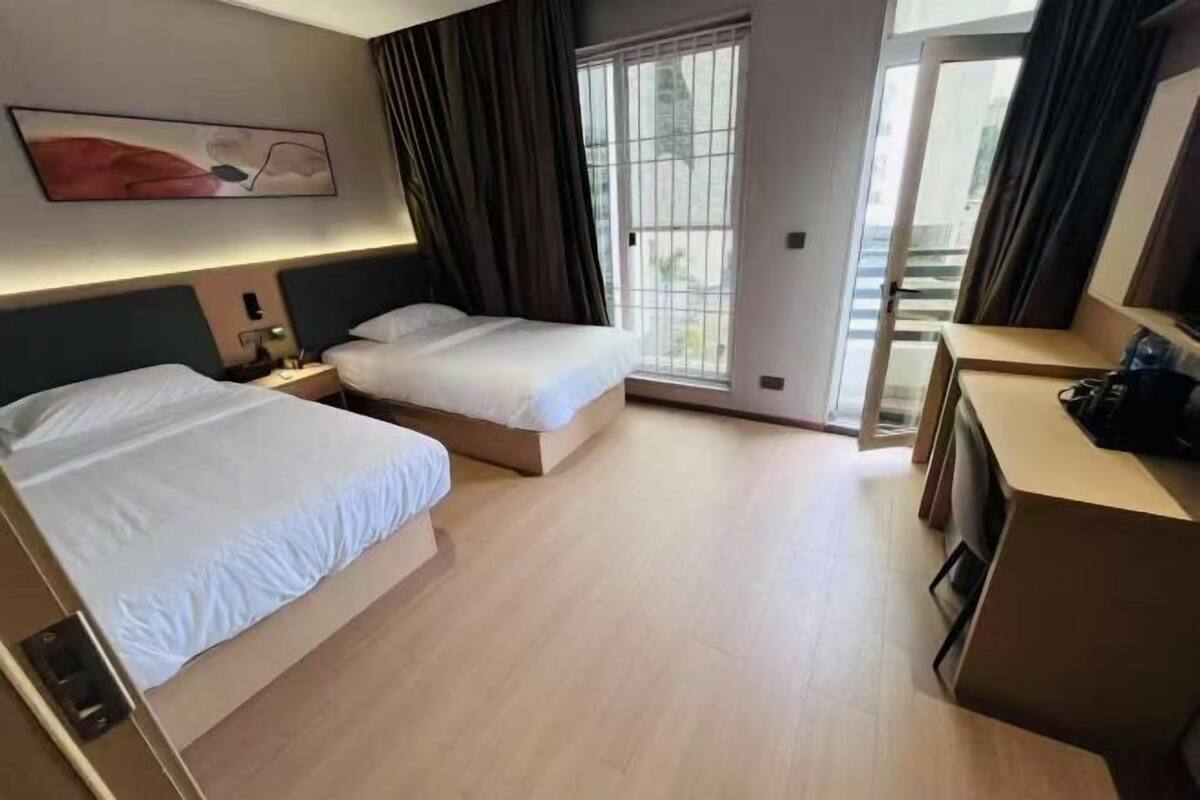 A hotel room with two beds, a desk, a chair, a window with curtains, and a painting on the wall.