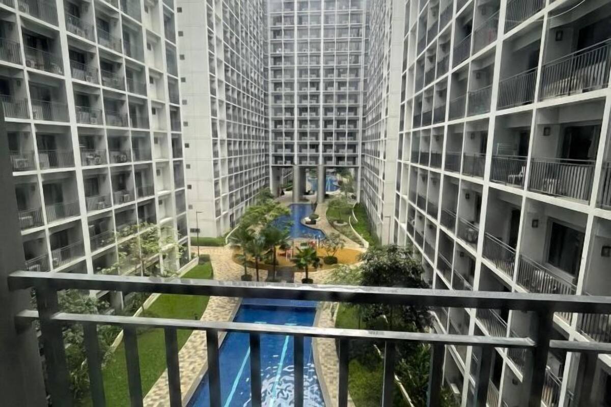 Un immeuble résidentiel de grande hauteur doté d’une cour intérieure avec une piscine, entourée de verdure et traversée par un petit pont.