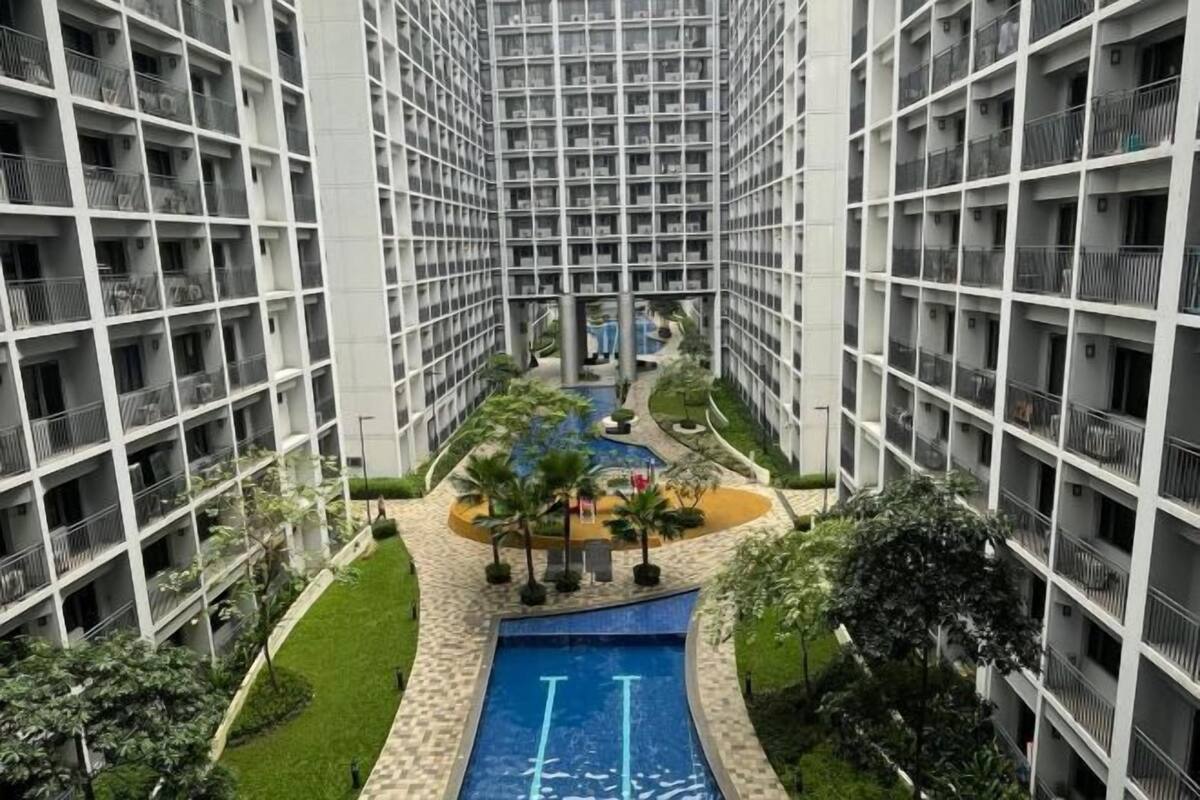 Un immeuble de grande hauteur doté de nombreux balcons, d’une piscine centrale et entouré de verdure.