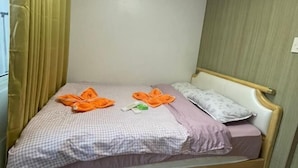 A single bed with a checkered bedspread, two orange towels, a white pillow, and a wooden headboard. - Coast Apartment (Pasay)