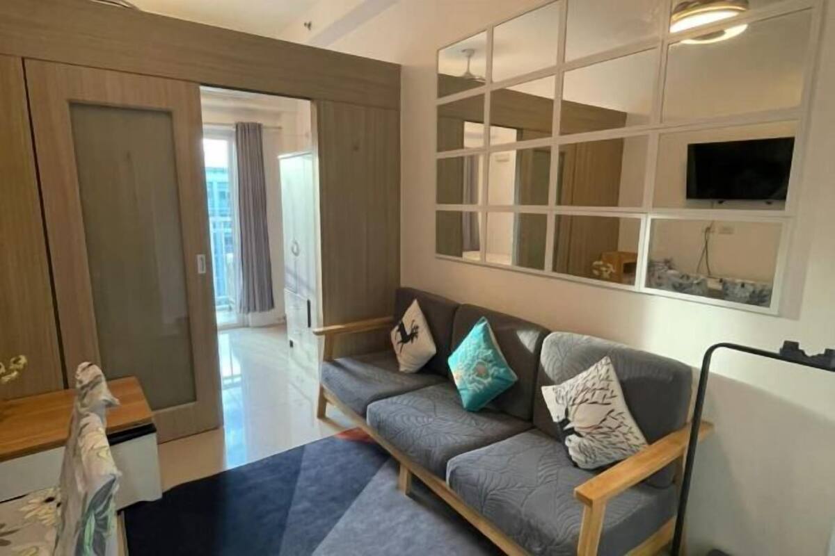 Un salon moderne avec un canapé, des coussins, un téléviseur et une fenêtre.