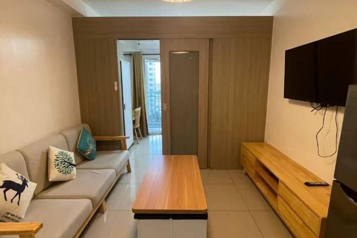Un salon moderne avec un canapé, une table basse en bois, un téléviseur fixé au mur et un banc en bois.