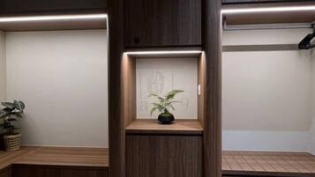 Habitación de hotel con un banco de madera, un estante pequeño con una planta y una pared con un panel decorativo.