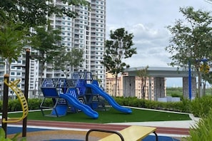A playground with slides and climbing structures, surrounded by greenery and a tall residential building in the background. - Urban Suites Jelutong 3BR Apartment with Infinity Pool · Near George Town · 18min to Airport (George Town)