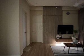 A living room with a flat-screen TV, a wooden cabinet, and a small table with a plant. - Urban Suites Jelutong 3BR Apartment with Infinity Pool · Near George Town · 18min to Airport (George Town)