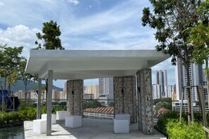 A covered outdoor area with stone pillars and white planters, overlooking a cityscape with high-rise buildings. - Urban Suites Jelutong 3BR Apartment with Infinity Pool · Near George Town · 18min to Airport (George Town)