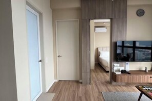A hotel room with a bed, a TV, a desk, and a view of the city. - Urban Suites Jelutong 3BR Apartment with Infinity Pool · Near George Town · 18min to Airport (George Town)