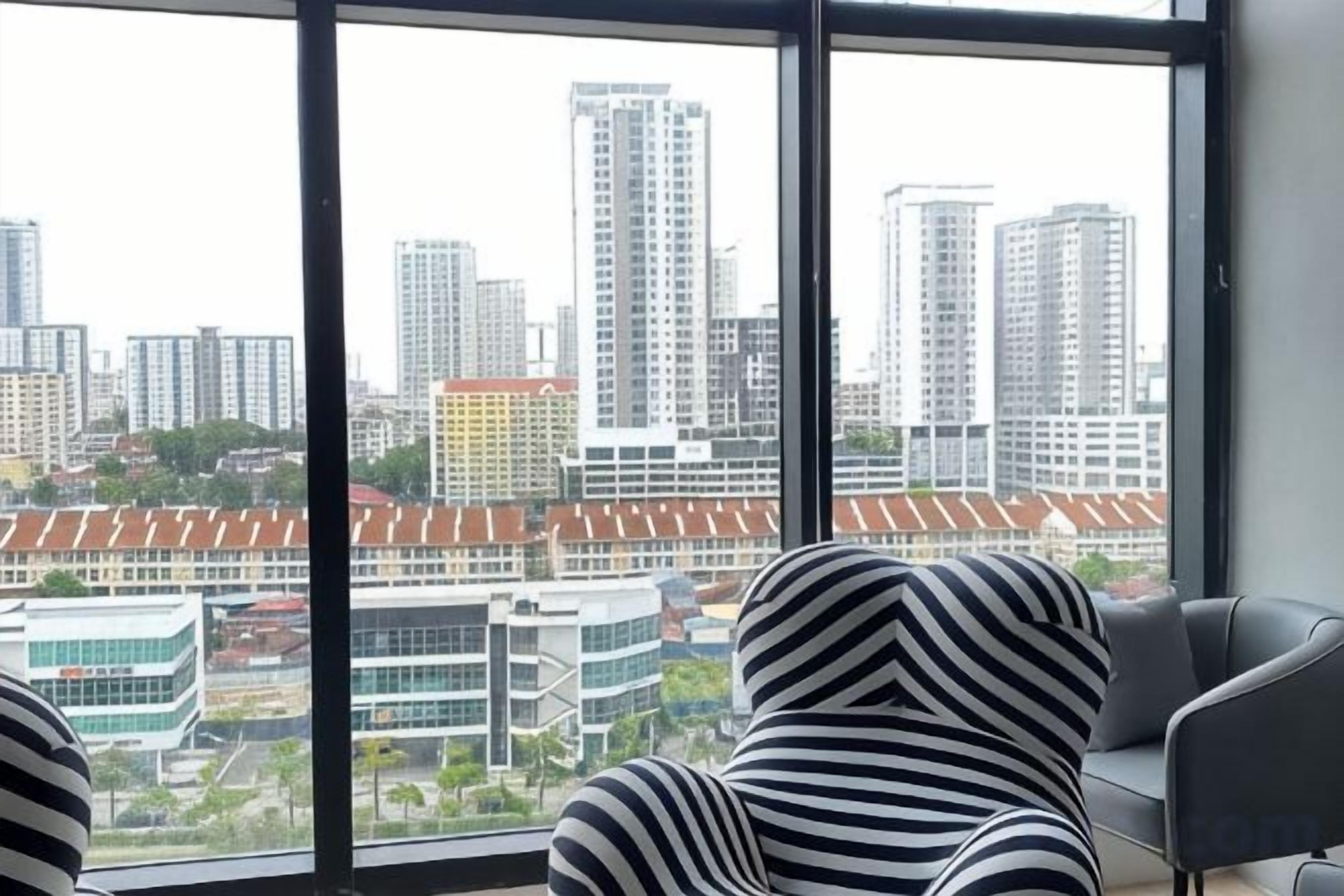 A room with a large window offering a cityscape view, a striped chair, and a modern sofa.