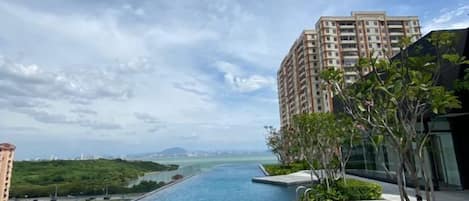 A residential building with a swimming pool, greenery, and a view of the sea.