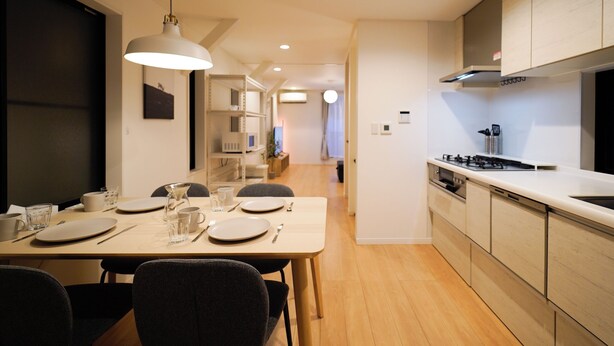 A modern kitchen with wooden cabinets, a dining table set for four, and a visible stove. - Satellite Hotel Roppongi 2nd (Tokyo)