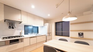 A modern kitchen with a dining area, featuring light wood cabinetry, a built-in oven, and a large window providing natural light. - Satellite Hotel Roppongi 2nd (Tokyo)