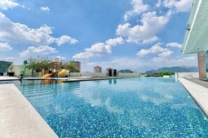A swimming pool with clear water, surrounded by buildings and a mountain view.