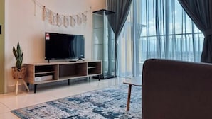 Ett modernt vardagsrum med en platt-TV på ett träställ, en krukväxt och ett stort fönster med gardiner.