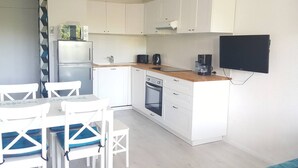 Een functionele keuken met witte kasten, een inbouwoven, een koffiezetapparaat en een flatscreen televisie aan de muur.