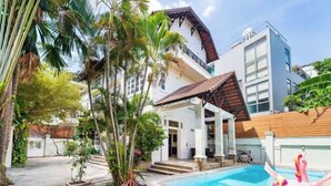 Une maison moderne dotée d’une piscine, entourée d’une végétation luxuriante et de palmiers.