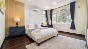 Une chambre à coucher comprenant un lit, une table de chevet, une lampe, un appareil de climatisation, une fenêtre avec des rideaux et une vue sur la verdure à l’extérieur.