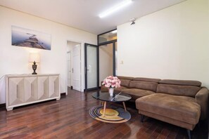 Ein Wohnzimmer mit braunem Sofa, einem Glastisch mit Blumenvase, einem weißen Schrank und einem Gemälde an der Wand.