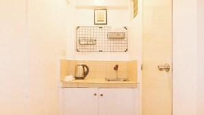 Une petite kitchenette équipée d’une machine à café, d’un évier et d’une étagère à motifs en forme de quadrillage, placée au-dessus de l’évier.