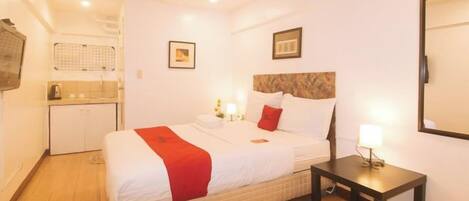 A hotel room with a bed, bedside table, and a small desk.