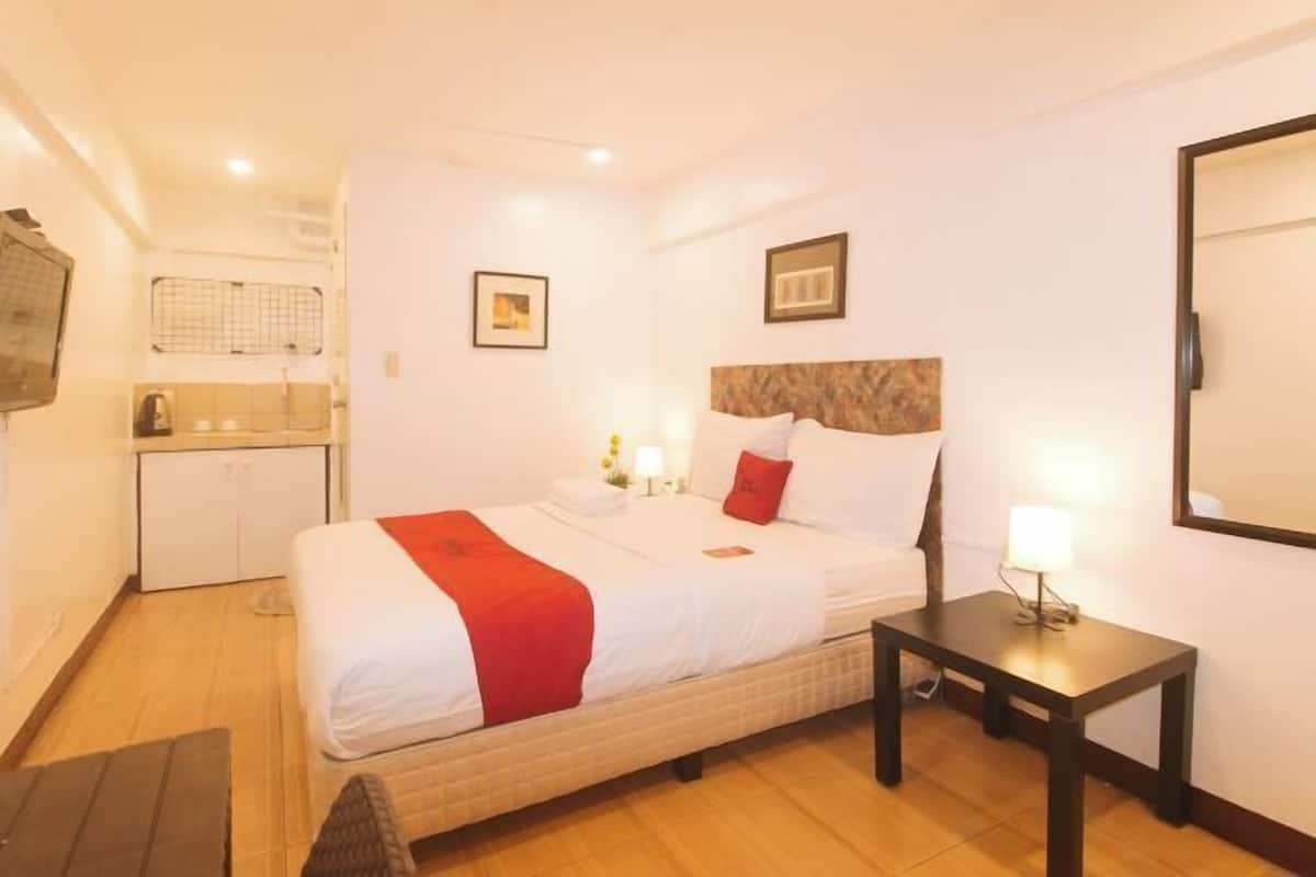 Een hotelkamer met een bed, nachtkastje en een kleine kitchenette.