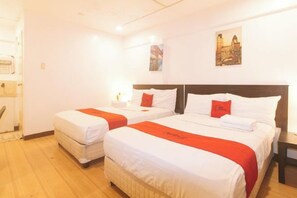 Una habitación de hotel con dos camas, cada una con ropa de cama blanca y detalles naranja, suelo de madera y un cuadro de un paisaje urbano en la pared.