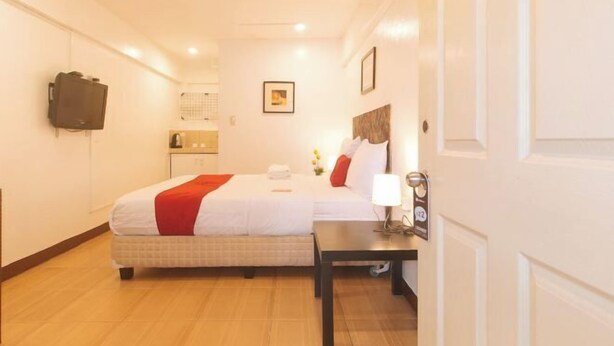 Une chambre d’hôtel comprenant un lit, une table de chevet, une lampe, un téléviseur fixé au mur et une porte avec une poignée.