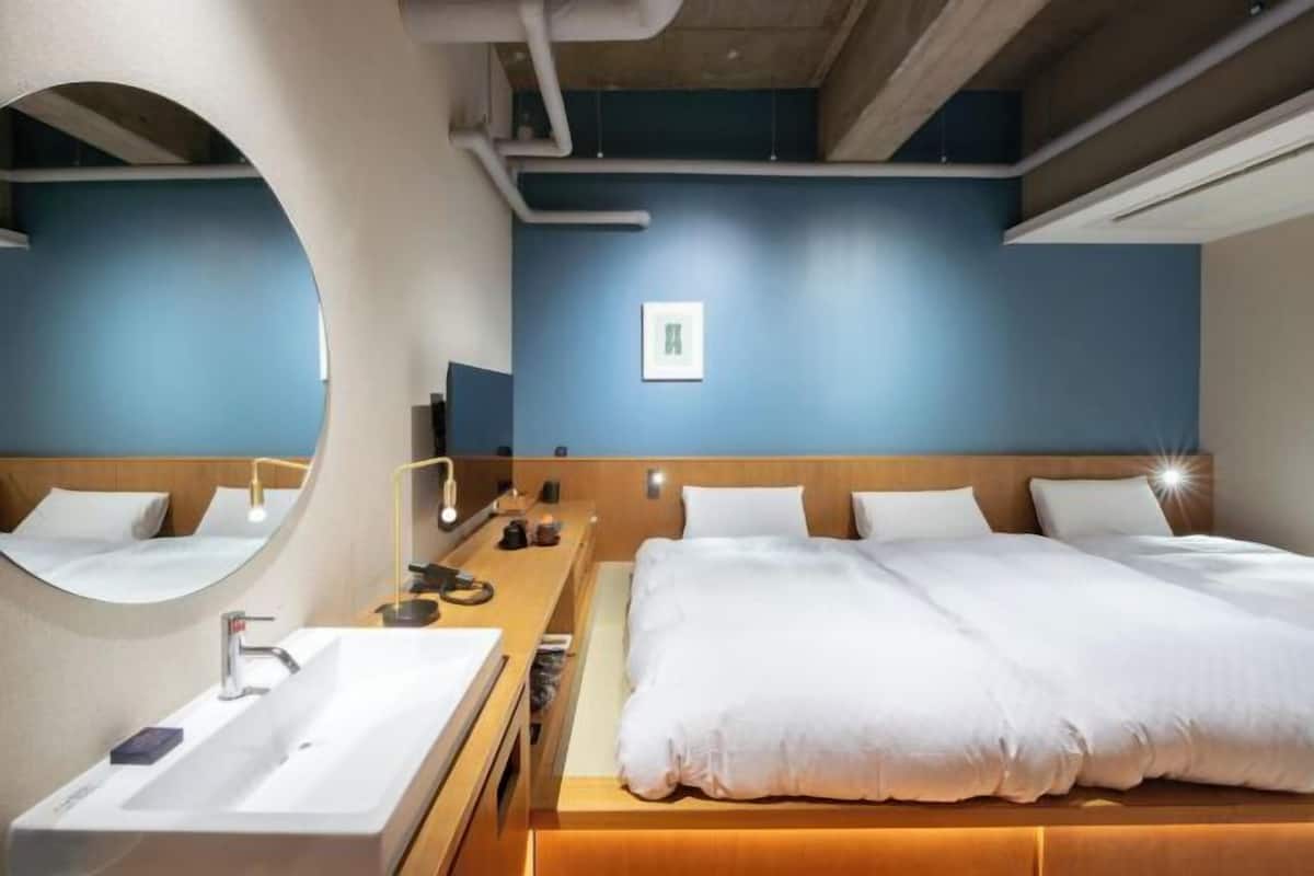Une chambre d’hôtel moderne avec un grand lit, un miroir rond, une table de chevet et un téléviseur fixé au mur.