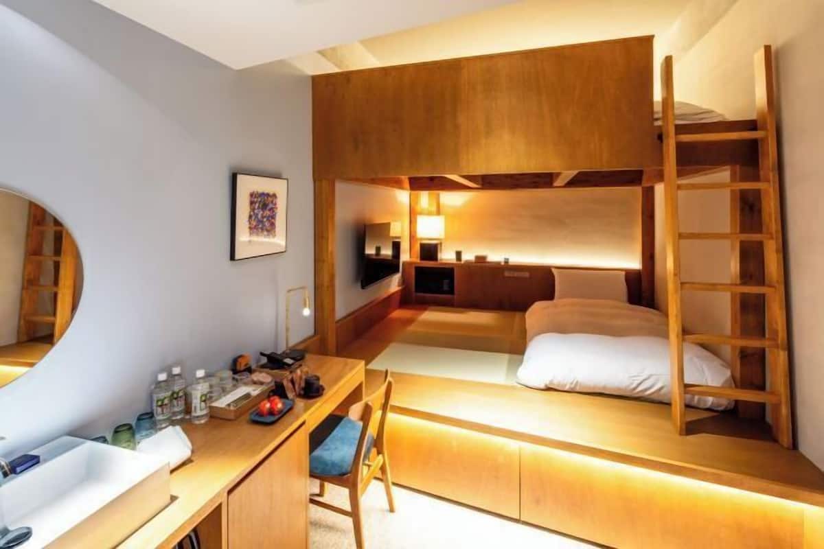 Une petite chambre comprenant un lit superposé, un bureau avec une chaise, un miroir et une petite étagère contenant des articles de toilette.