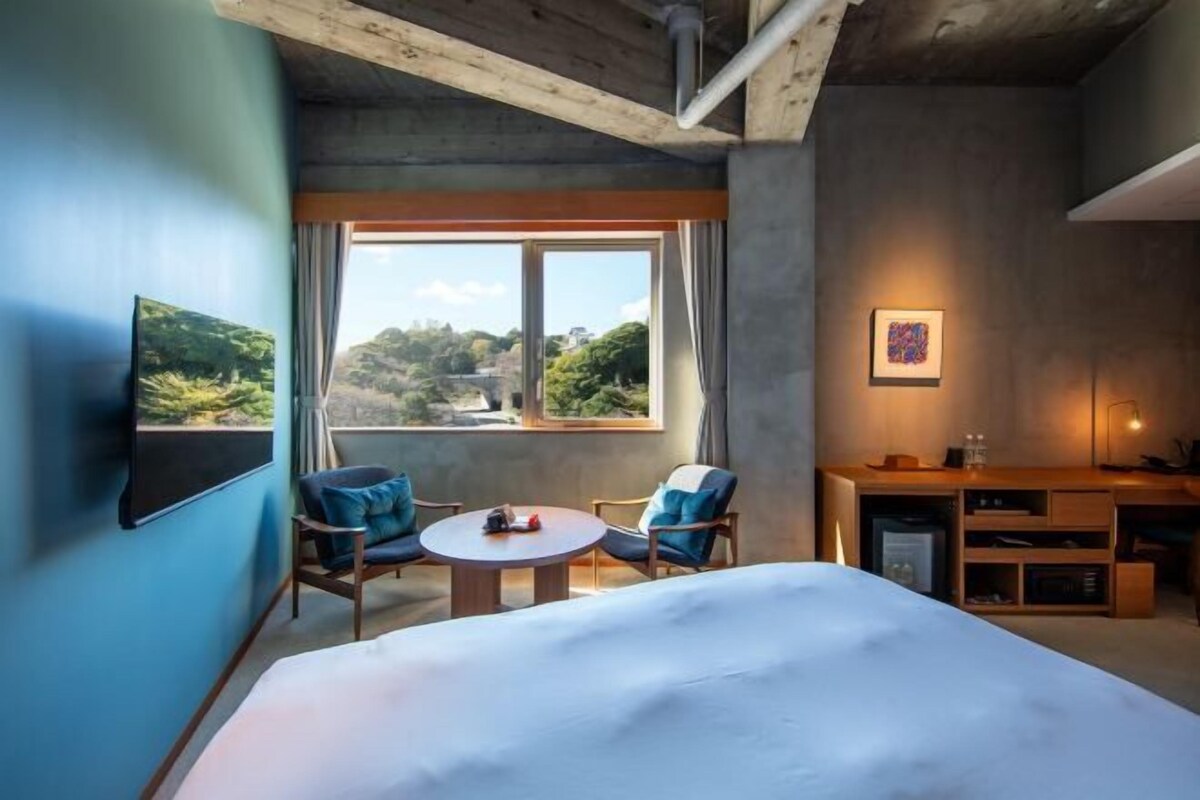 Une chambre d’hôtel comprenant un lit, deux chaises, une petite table, un bureau et un téléviseur fixé au mur.