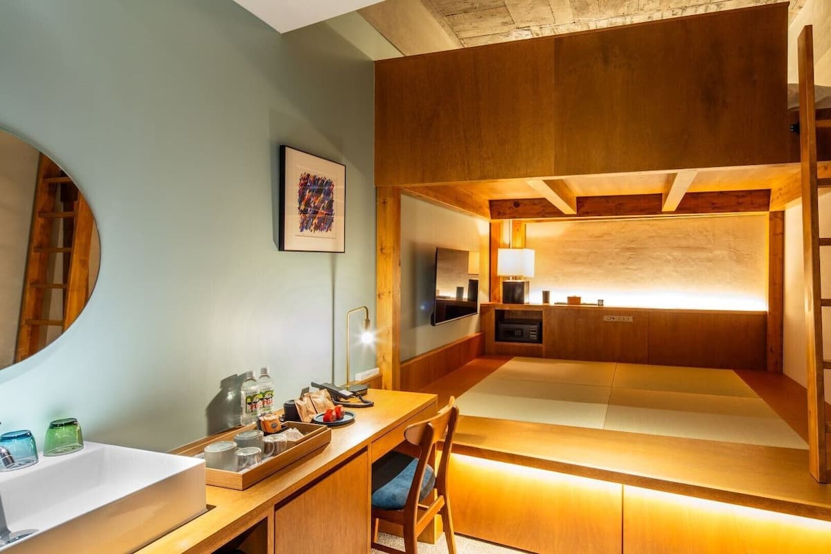 Une petite pièce comprenant un lit superposé, un bureau avec une chaise, un miroir et un tableau encadré accroché au mur.