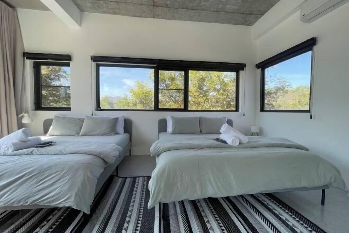 Une chambre avec deux lits, de grandes fenêtres et un tapis à motifs.