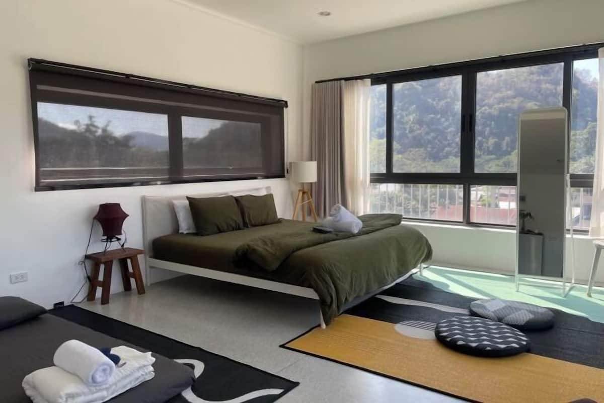 Une chambre d’hôtel moderne équipée d’un lit, d’un bureau, d’une chaise, d’une lampe et d’une grande fenêtre donnant sur un beau paysage.