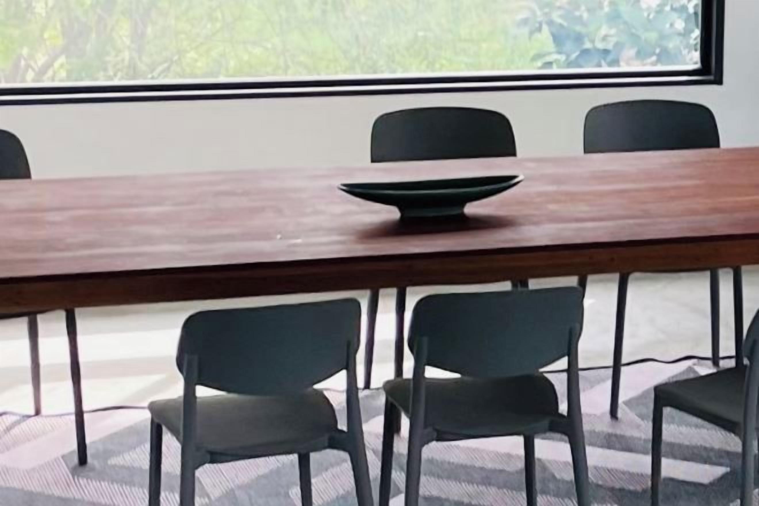 A conference table with a bowl, four chairs, and a window with a view of greenery.