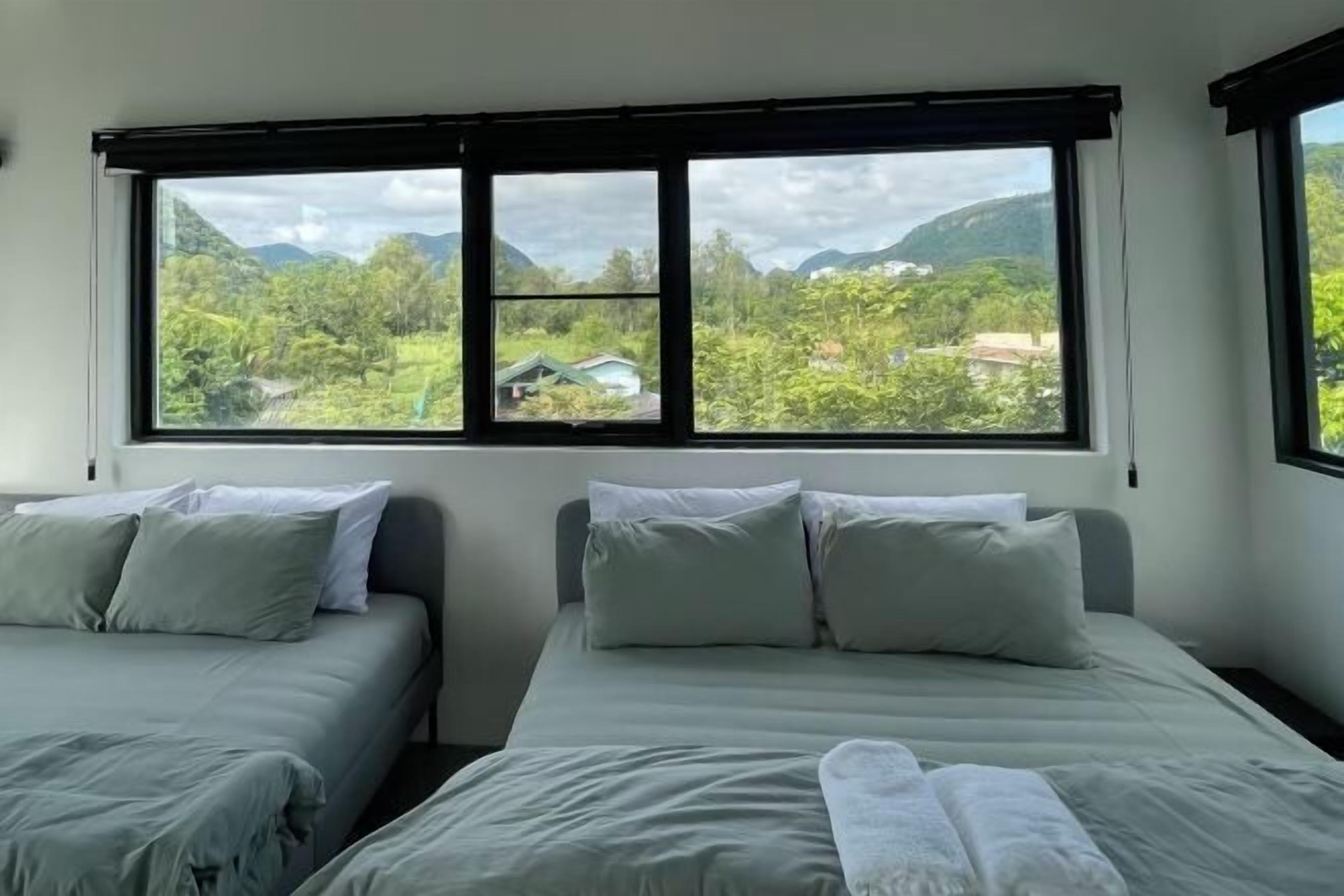Una habitación con dos camas, un ventanal con vistas a zonas verdes y montañas, y un diseño sencillo y limpio.