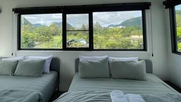 Una habitación con dos camas, un ventanal con vistas a zonas verdes y montañas, y un diseño sencillo y limpio.