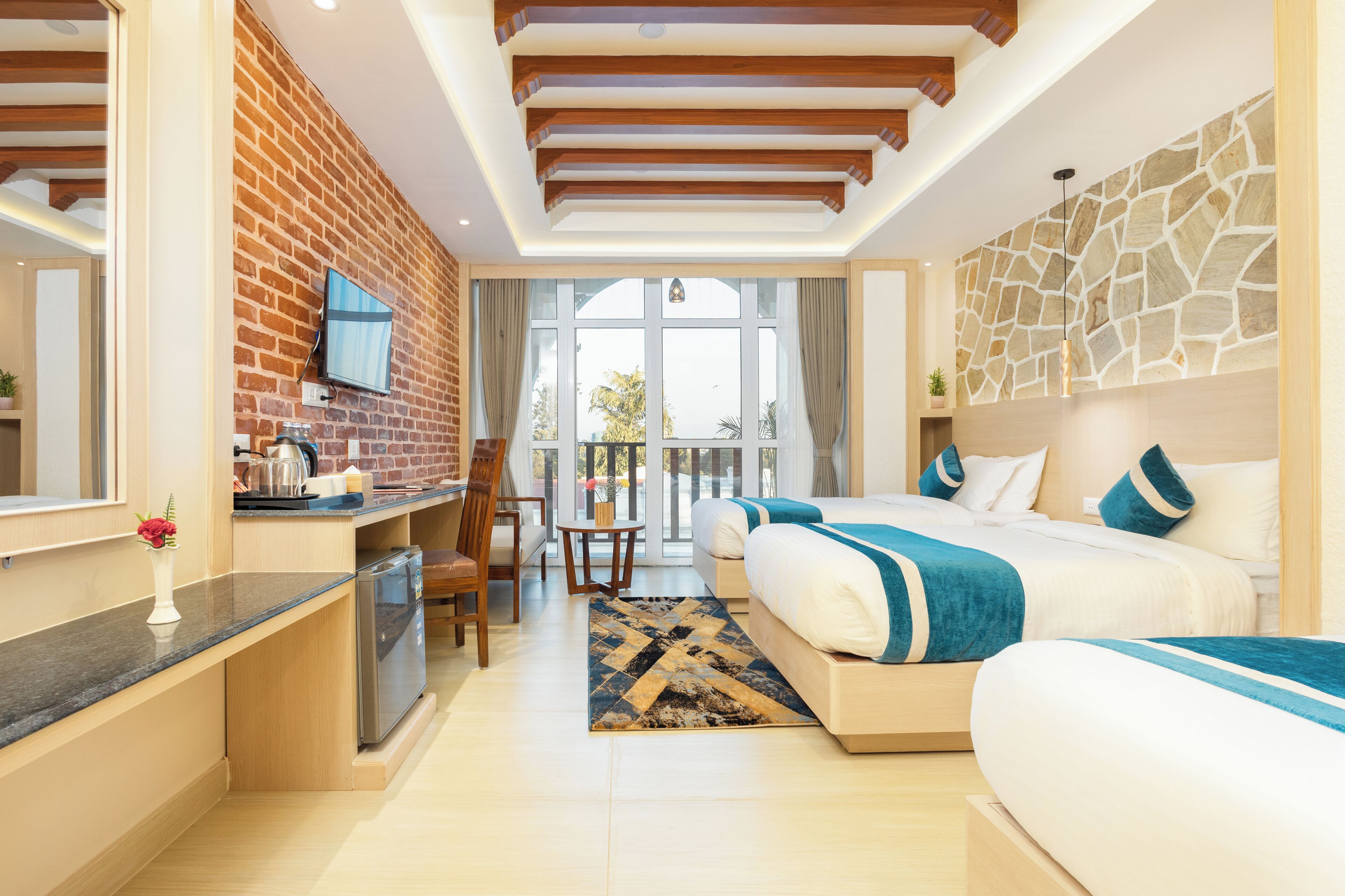 A hotel room with a brick wall, a large bed, a desk with a chair, a small table, and a view of the outdoors.