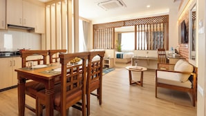 A modern kitchen with wooden cabinetry, a dining table with chairs, a sofa, and a TV mounted on the wall. - Tulsi Kathmandu Hotel (Kathmandu)