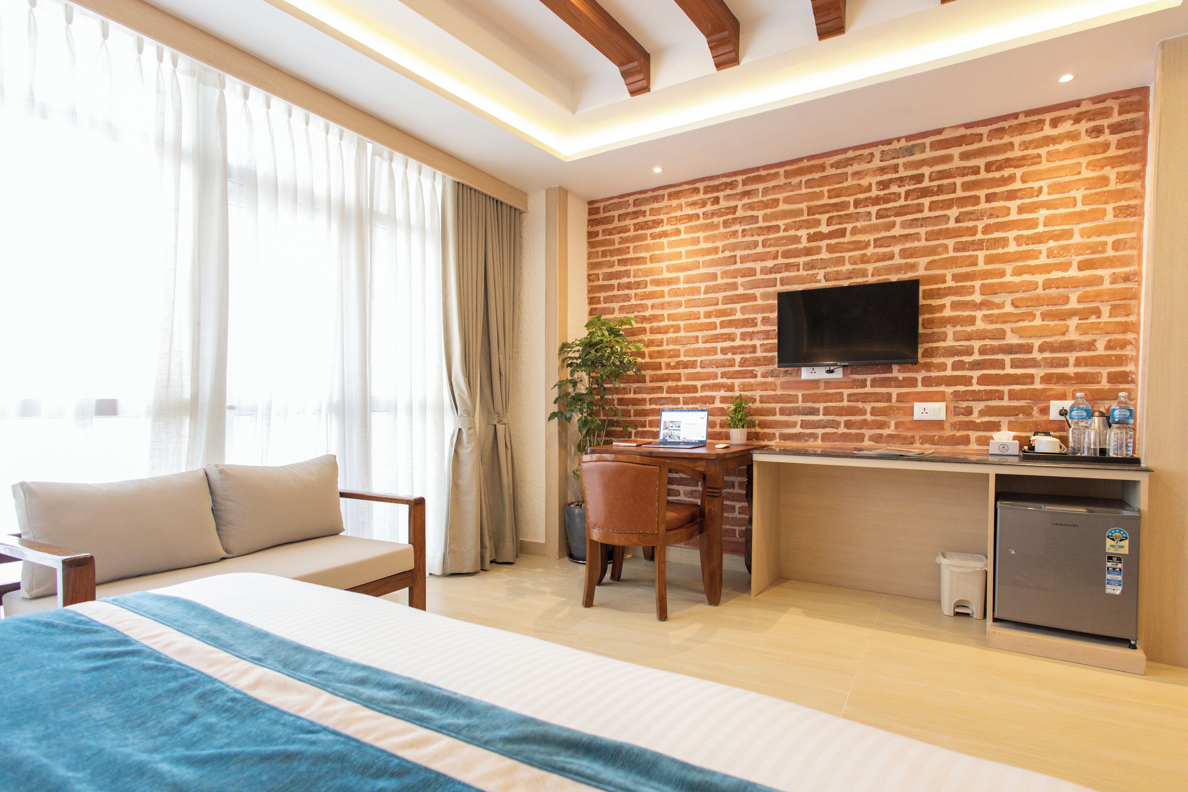 Una camera d'albergo con un letto, una scrivania con un computer, una televisione fissata a una parete in mattoni e un piccolo frigorifero.