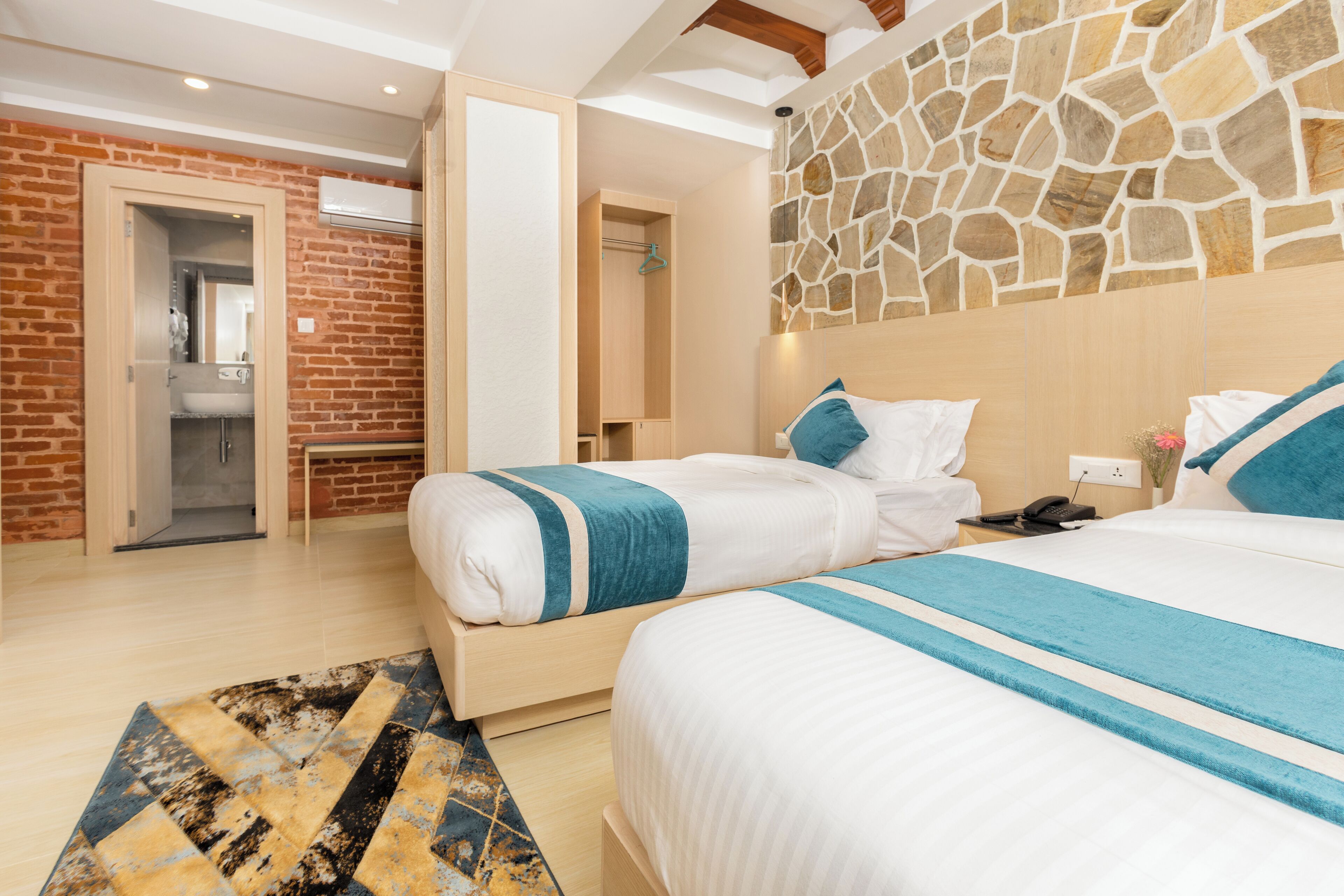 A hotel room with two beds, a stone wall, a brick wall, and a bathroom visible through an open door.