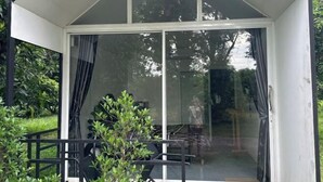 A modern glass-enclosed room with a sliding door, a small table, and chairs, surrounded by greenery. - INK-PHA GARDENVIEW RESORT (Noen Maprang)