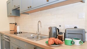 A kitchen with a double sink, a kettle, a toaster, and a plate of croissants. - Swallow Studio (Cheltenham)