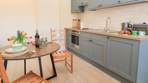 A compact kitchen with grey cabinets, a wooden dining table, and a small island with a sink and toaster. - Swallow Studio (Cheltenham)